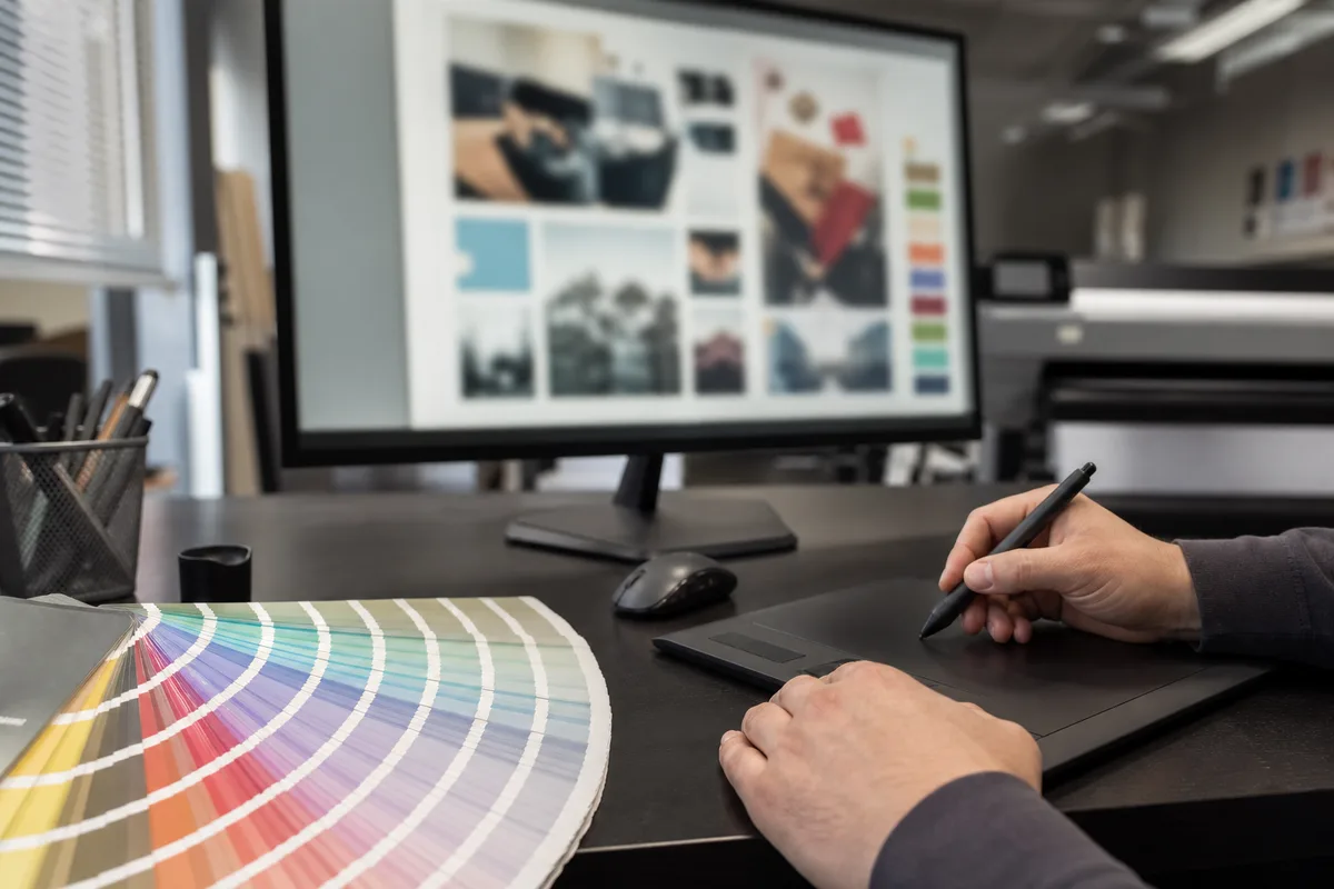 Poste de prépresse et PAO avec écran affichant une mise en page, nuancier Pantone et tablette graphique